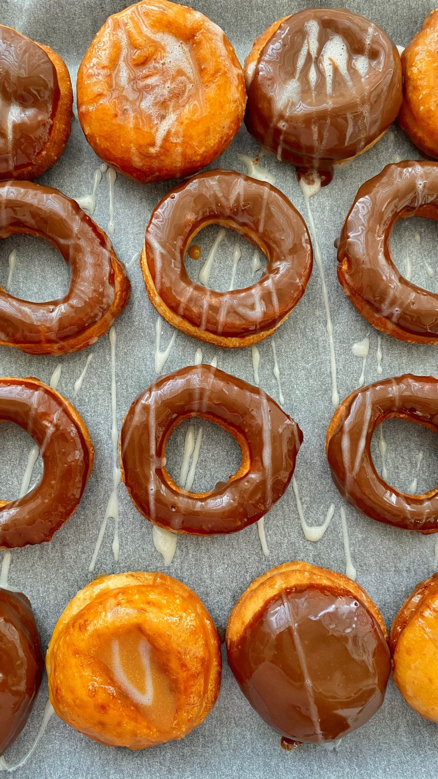 Freshly glazed chocolate donuts cooling in rows, glaze still glossy.